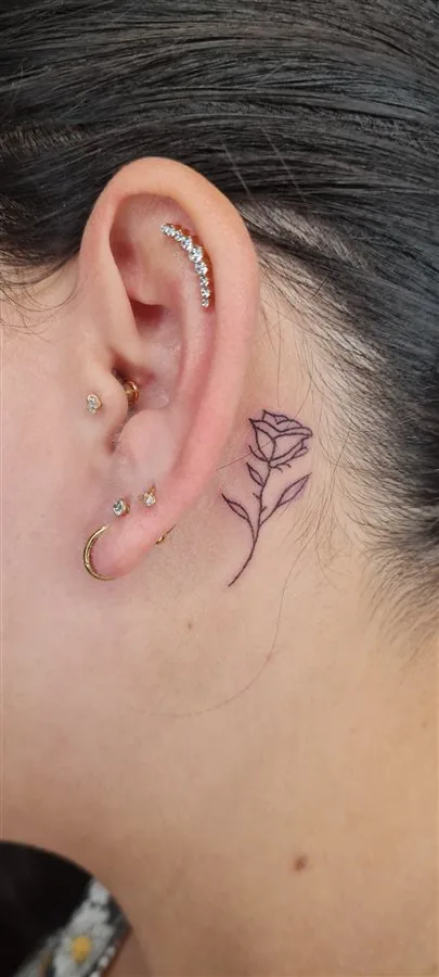 Piercing na orelha e tatuagem fine line de rosa